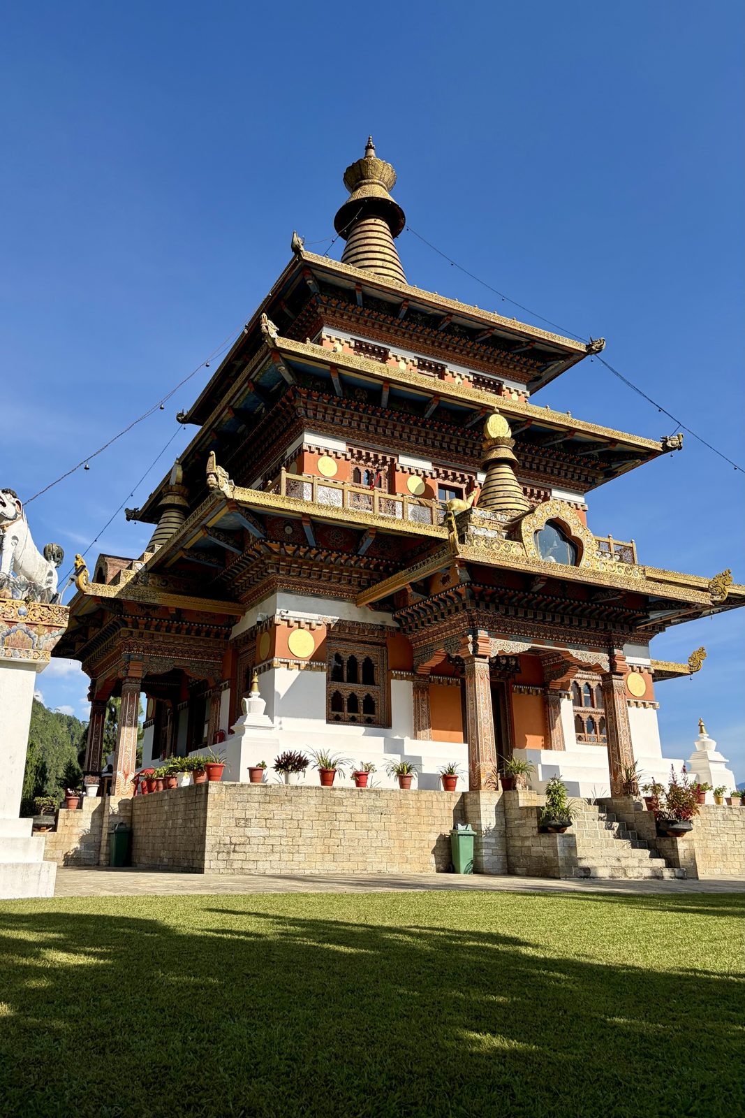 Dezelfde tempel vanaf een hoek, met zicht omhoog op de verdiepingen met gesneden en beschilderde dakranden, gouden dakboorden en de spits tegen een diepblauwe hemel.