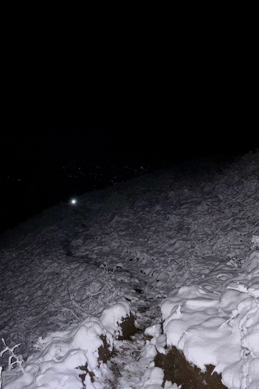 Een pad in de sneeuw in het donker, verlicht door een hoofdlamp.
