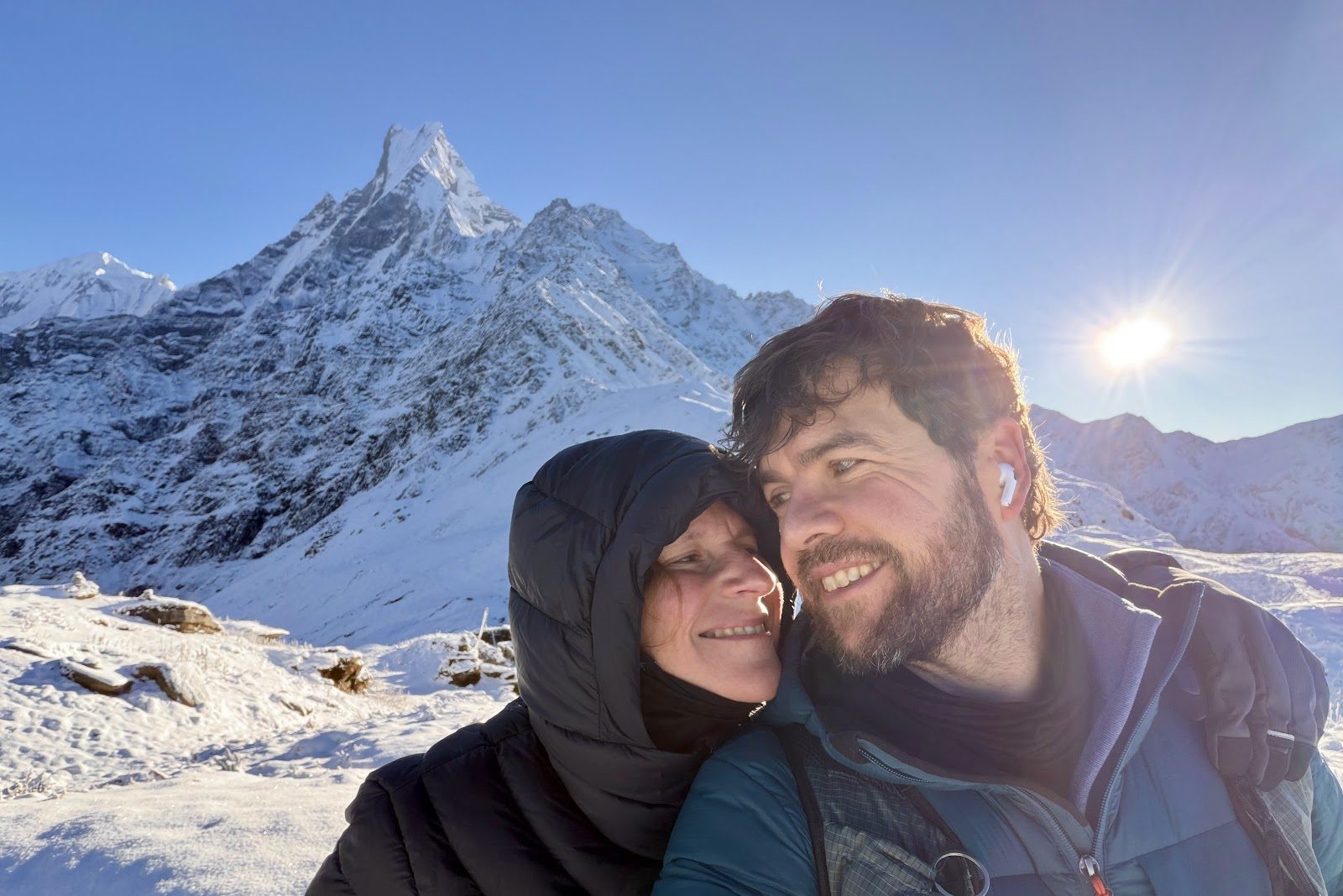 Twee van ons in donsjassen, wang aan wang, met de besneeuwde Machhapuchhre en de zon erachter.