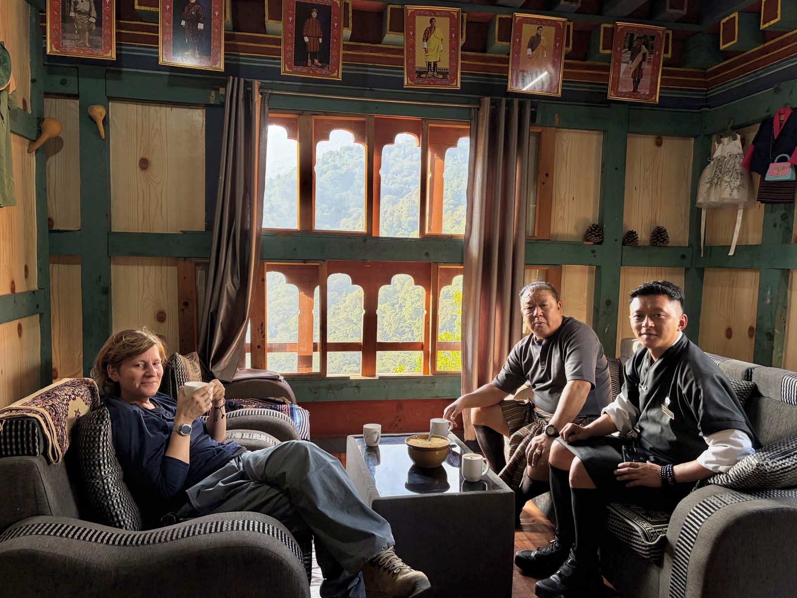 Jack, onze chauffeur, in een gestreepte gho, en Dawa, onze gids, in een zwarte gho, met iemand van ons met een kop thee in de hand, in zetels rond een lage tafel met mokken en een kom gepofte rijst, in een houten kamer met grote beschilderde vensters en een rij portretten van de koningen onder het plafond.